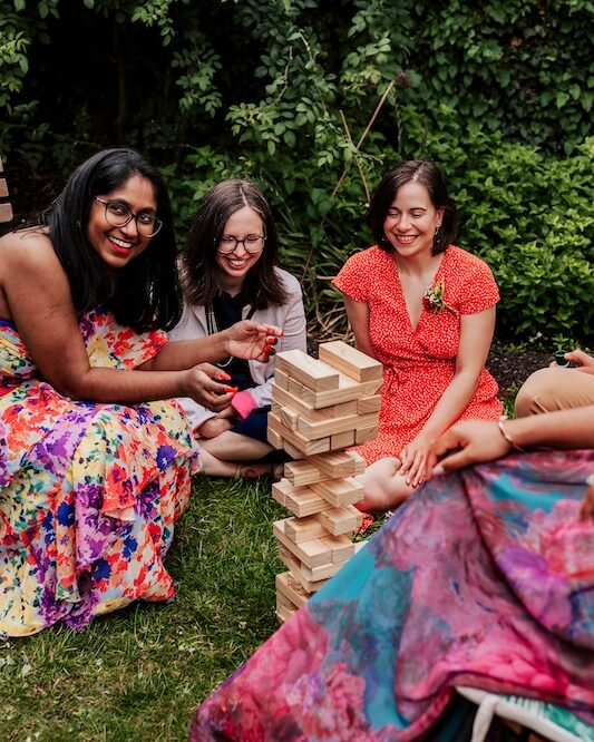 Guests gather around a large Jenga game on the lawn at No.4 Clifton Village, an outdoor wedding venue in Bristol. The scene is filled with laughter and friendly competition as everyone enjoys this light-hearted moment during the wedding reception. The lush greenery and cozy seating arrangements enhance the welcoming atmosphere, making this Clifton venue an ideal spot for a relaxed and fun-filled outdoor wedding.